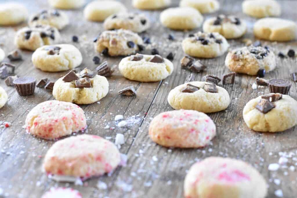 Variety of freshly baked cookies with chocolate chunks and sprinkles on a wooden surface.