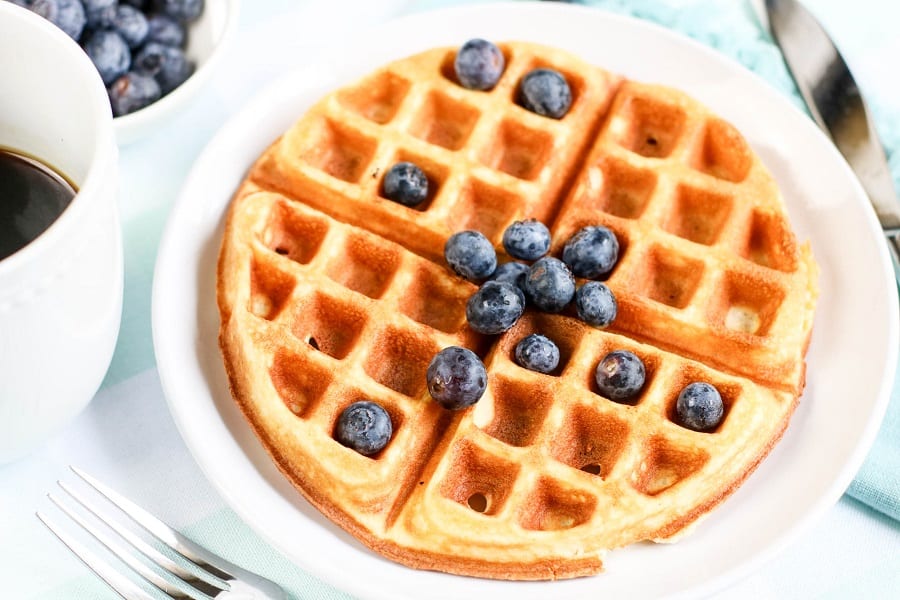 Golden brown waffle topped with fresh blueberries, accompanied by a cup of coffee, perfect for breakfast recipes.