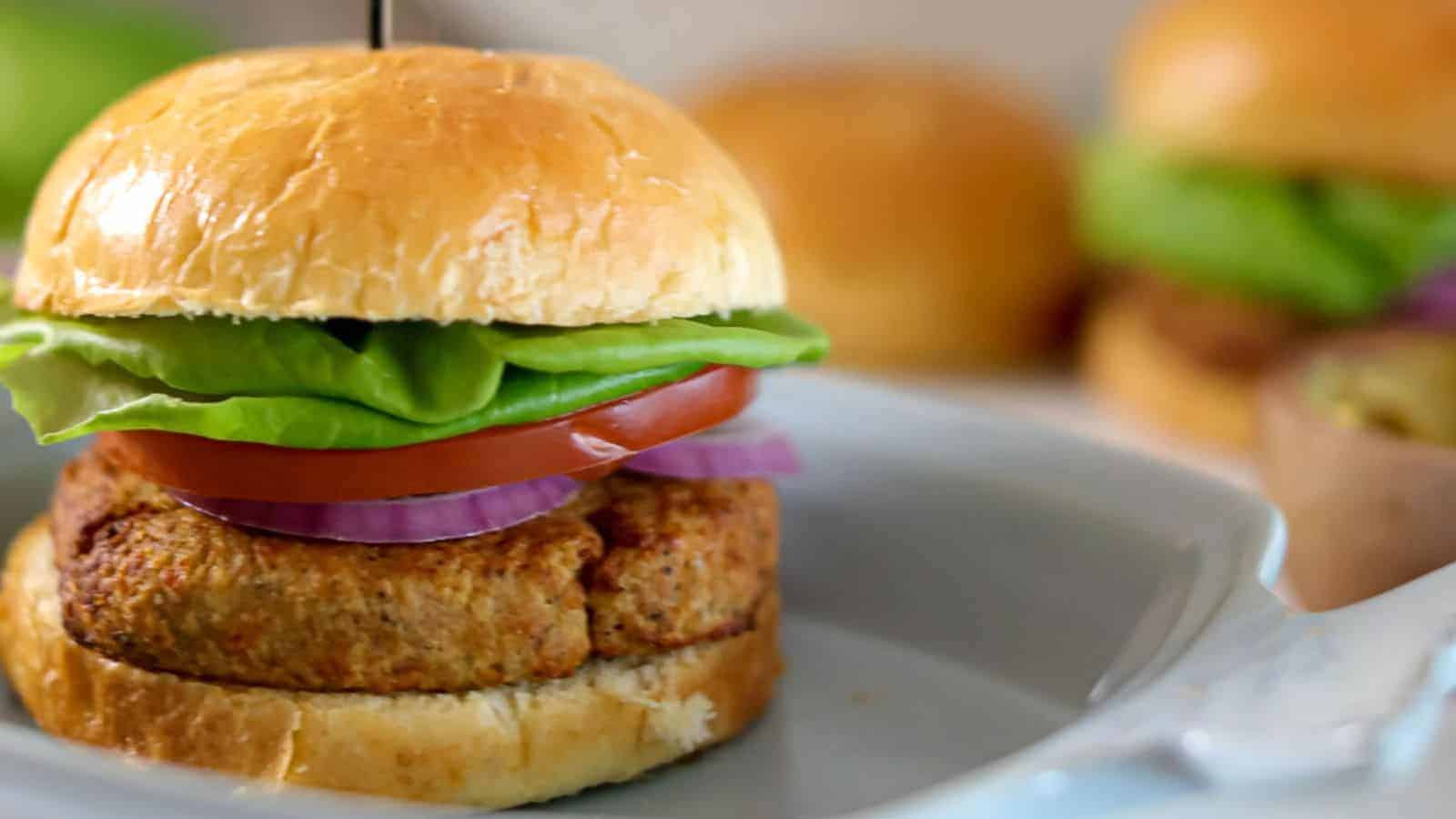 Tuna burger with lettuce, tomato, and onion on a bun, served on a white plate.