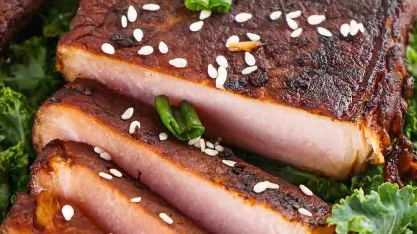 Close-up of sliced grilled pork belly garnished with sesame seeds and green chili, served on a bed of kale.