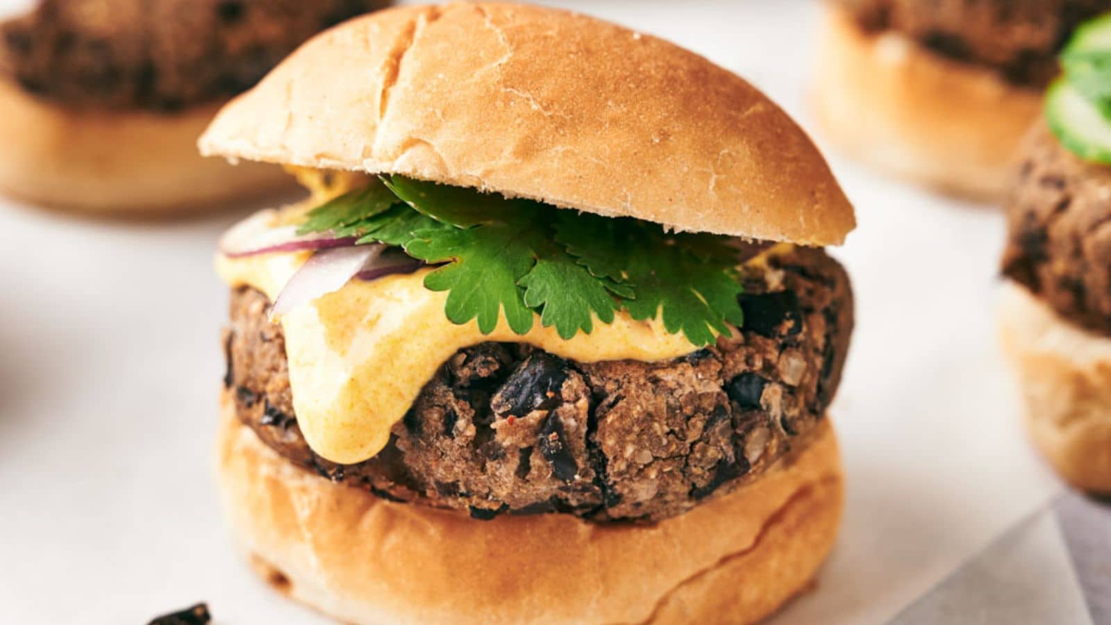 A black bean burger with a slice of cheese, cilantro, and red onion, served on a toasted bun.