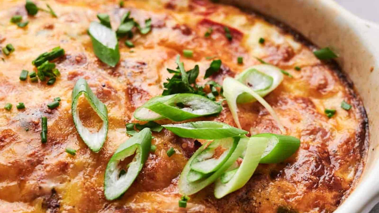 Breakfast casserole topped with melted cheese, garnished with sliced green onions and chopped herbs.