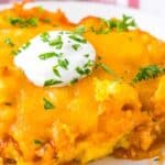 A serving of chicken tamale pie topped with a dollop of sour cream and garnished with chopped herbs on a white plate.