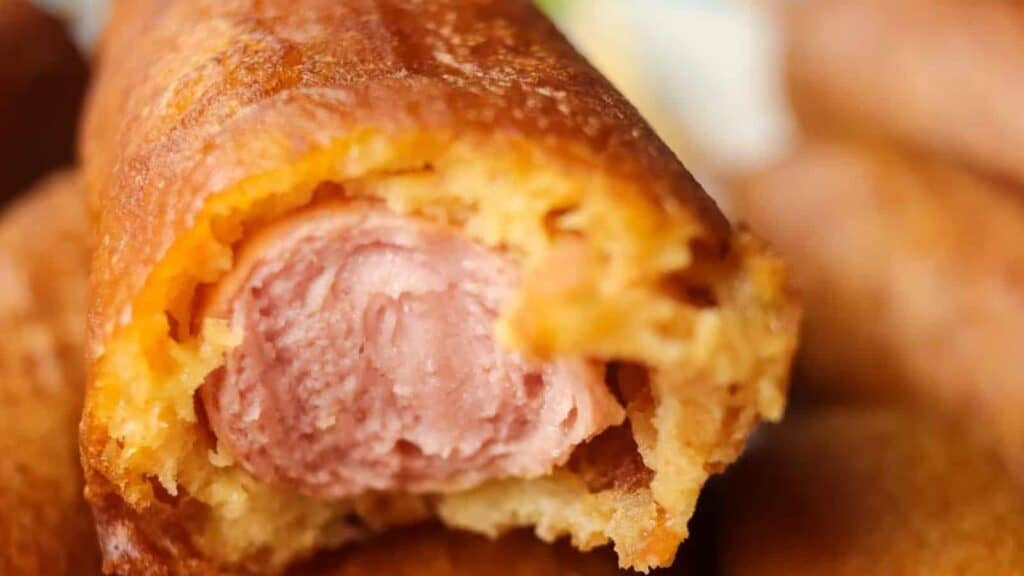 Close-up of a bitten corn dog exposing the hot dog inside with a crispy golden-brown exterior.