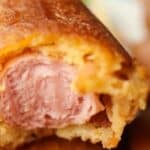 Close-up of a bitten corn dog exposing the hot dog inside with a crispy golden-brown exterior.