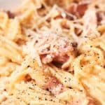 A close-up image of a creamy spaghetti carbonara sprinkled with grated parmesan and black pepper.