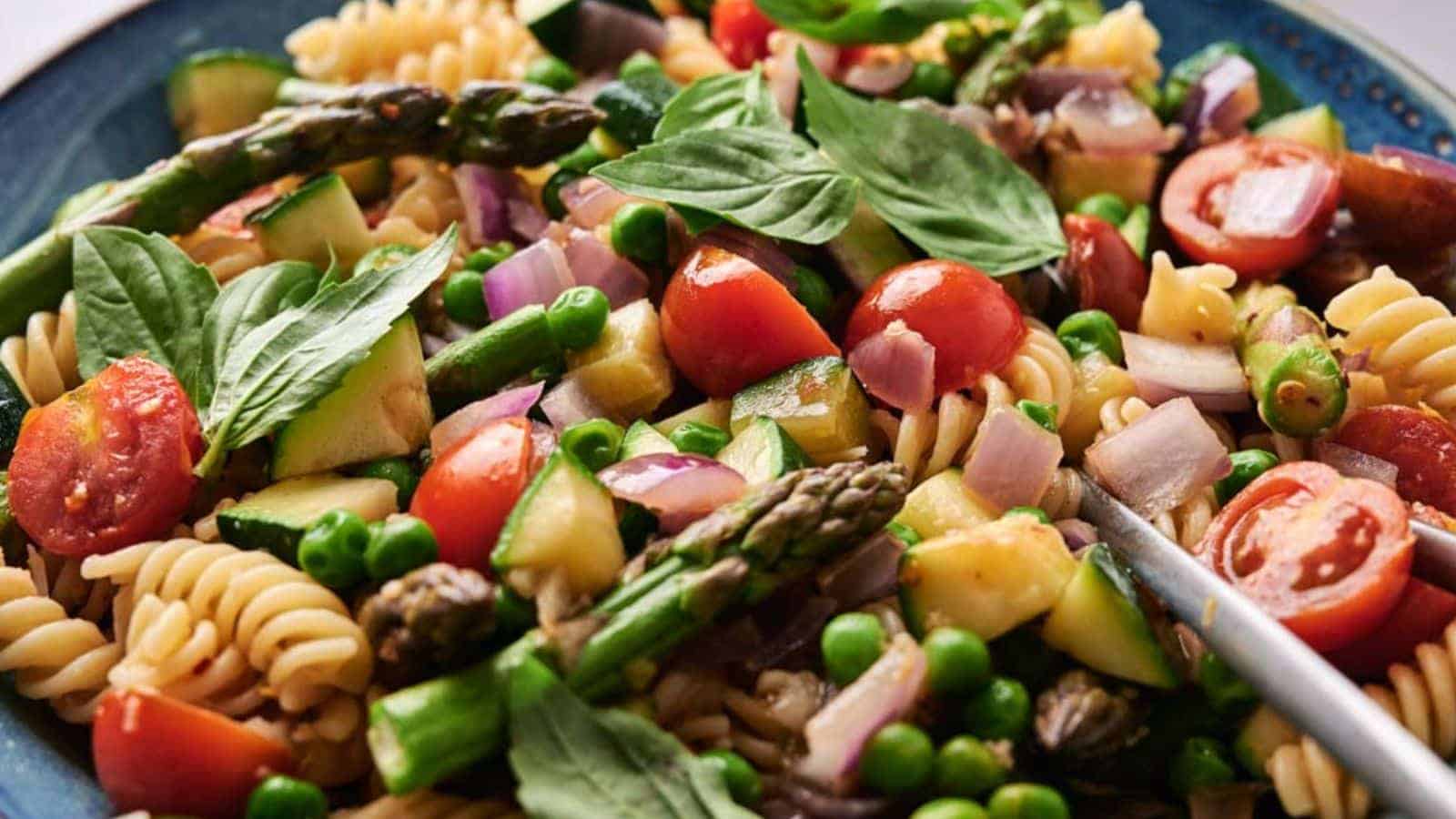 A colorful Pasta Primavera salad with cherry tomatoes, asparagus, peas, and spinach in a blue bowl.