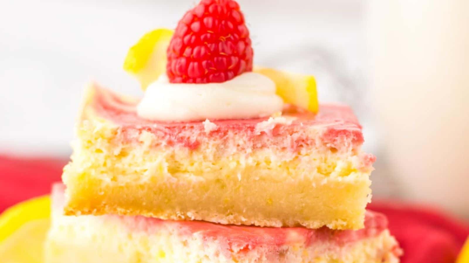 A close-up image of layered lemon raspberry cake slices topped with fresh raspberries and lemon zest.