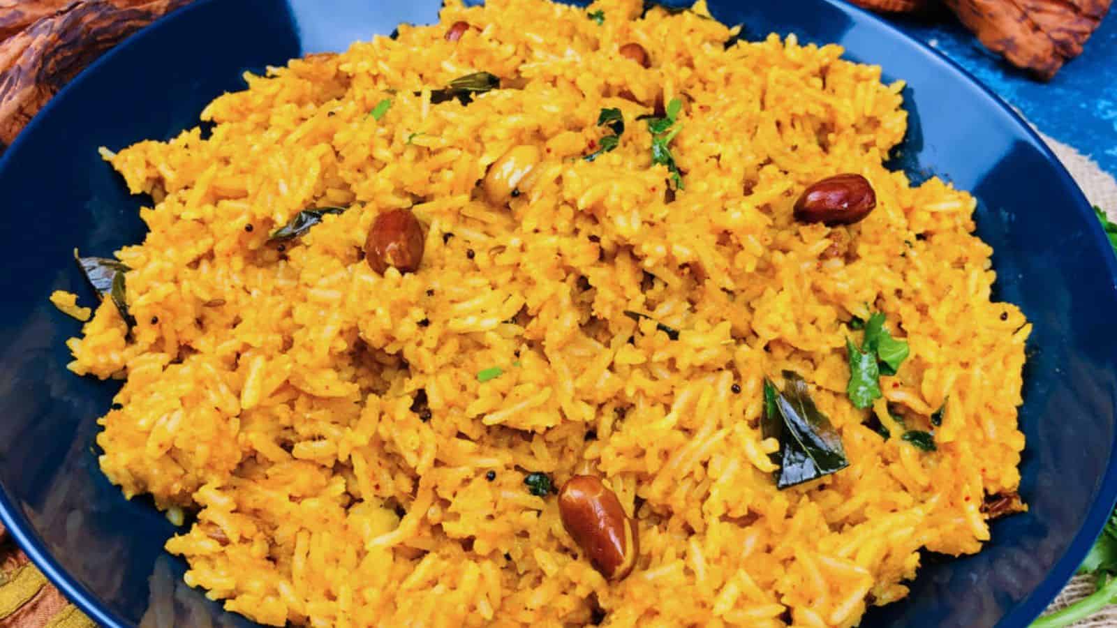 A close-up of a blue bowl filled with yellow spiced rice garnished with peanuts and herbs.