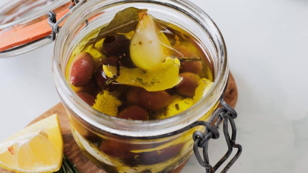 A jar of mixed olives marinated in oil with lemon and herbs.