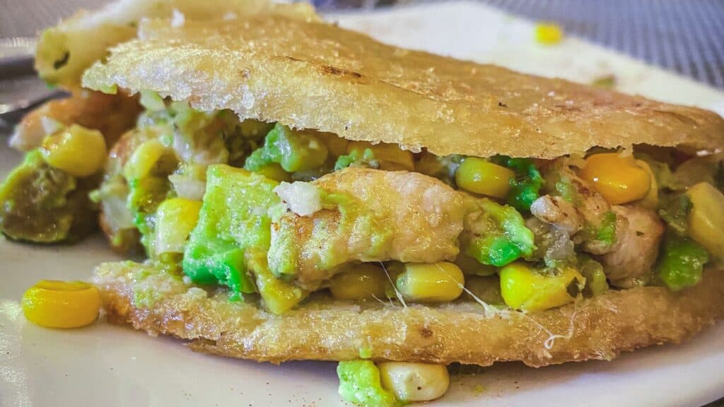 A chicken and avocado arepa with corn filling on a plate.