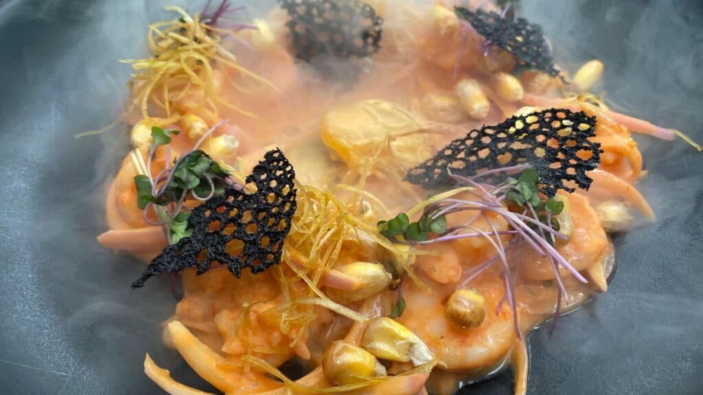 A gourmet shrimp dish garnished with microgreens, edible flowers, and crispy decorations, presented with a smoky effect.