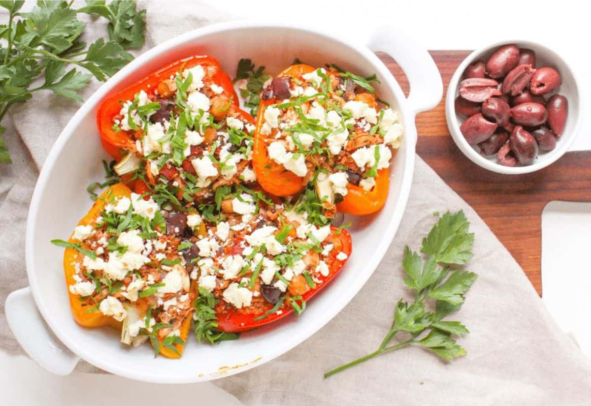 Bell peppers stuffed with chicken, feta, quinoa, and vegetables in an oval-shaped white baking dish.