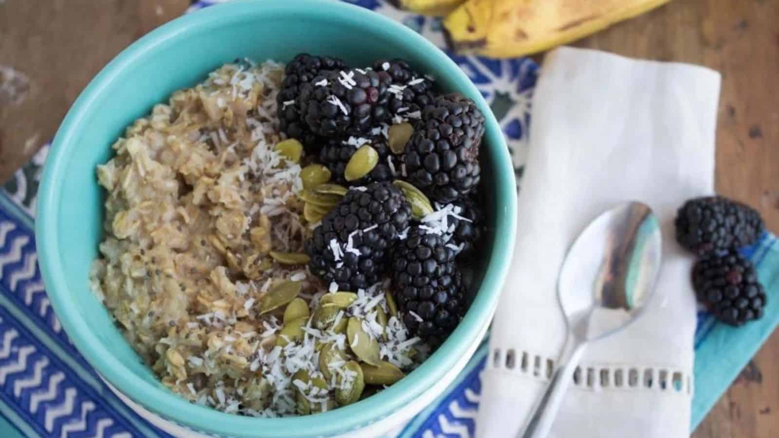 A bowl of banana oatmeal with blackberries, shredded coconut, and pumpkin seeds on top.