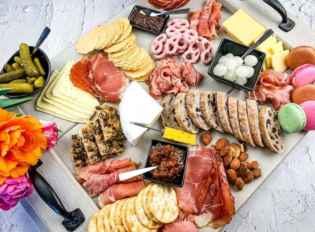 A charcuterie board with assorted meats, cheeses, nuts, pickles, and crackers, accompanied by a small bouquet of flowers.