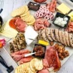 A charcuterie board with assorted meats, cheeses, nuts, pickles, and crackers, accompanied by a small bouquet of flowers.