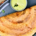 A folded, Mysore Masala Dosa on a dark plate served with a side of green chutney.