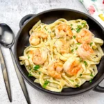 A bowl of olive garden creamy shrimp alfredo pasta served in a black bowl with a spoon.