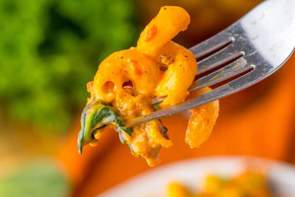A close-up of pasta with a creamy tomato sauce on a fork, with fresh basil, against a blurred background.