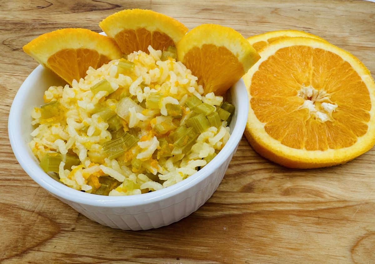 Bowl of rice with chopped celery and orange slices on a wooden table.