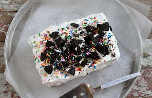 A homemade ice cream cake with oreo topping and colorful sprinkles on parchment paper.