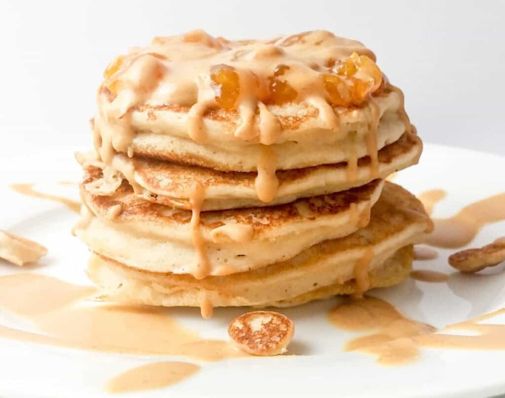 A stack of fluffy pancakes topped with caramel sauce and pecans on a white plate.