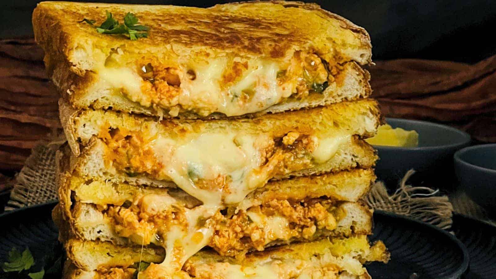 A Paneer Sandwich with melted cheese stretching between two halves, filled with a spicy minced meat mixture, served on a dark plate.