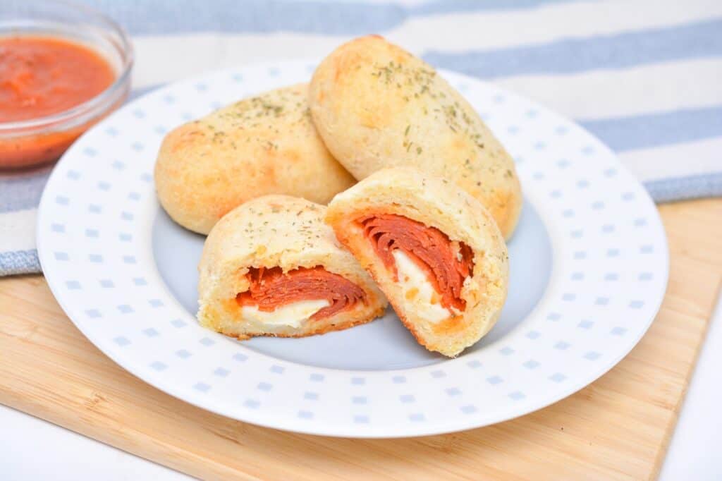 Pepperoni and cheese stuffed bread rolls served on a plate with a side of marinara sauce.