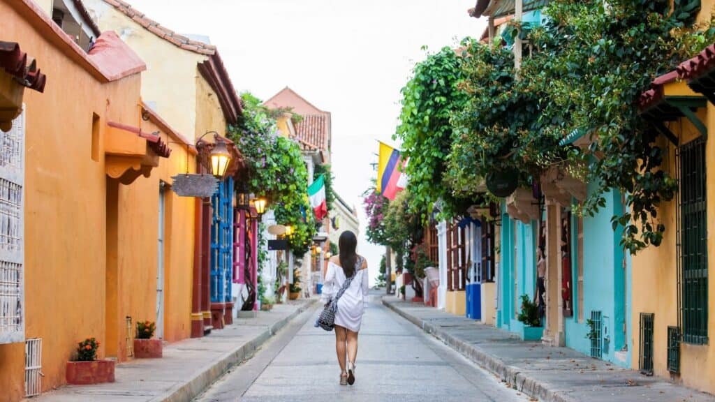 A woman walks down a vibrant street lined with colorful buildings and lush plants in cartagena, colombia.