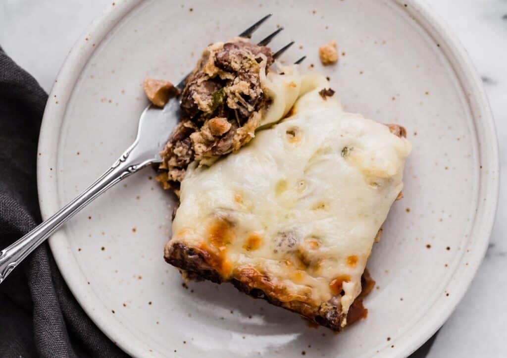 A slice of Philly cheese steak casserole on a plate, partially eaten with a fork.
