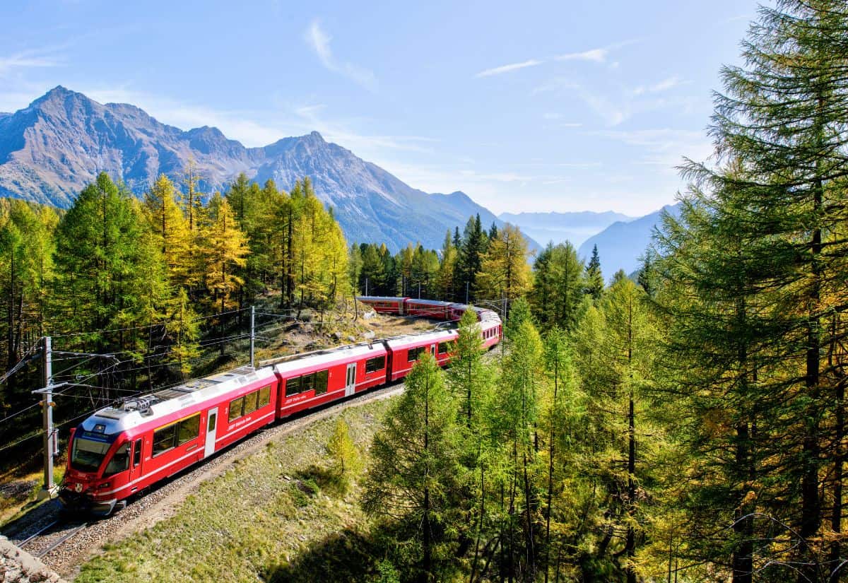 A red train traveling through a mountainous landscape with autumn foliage.