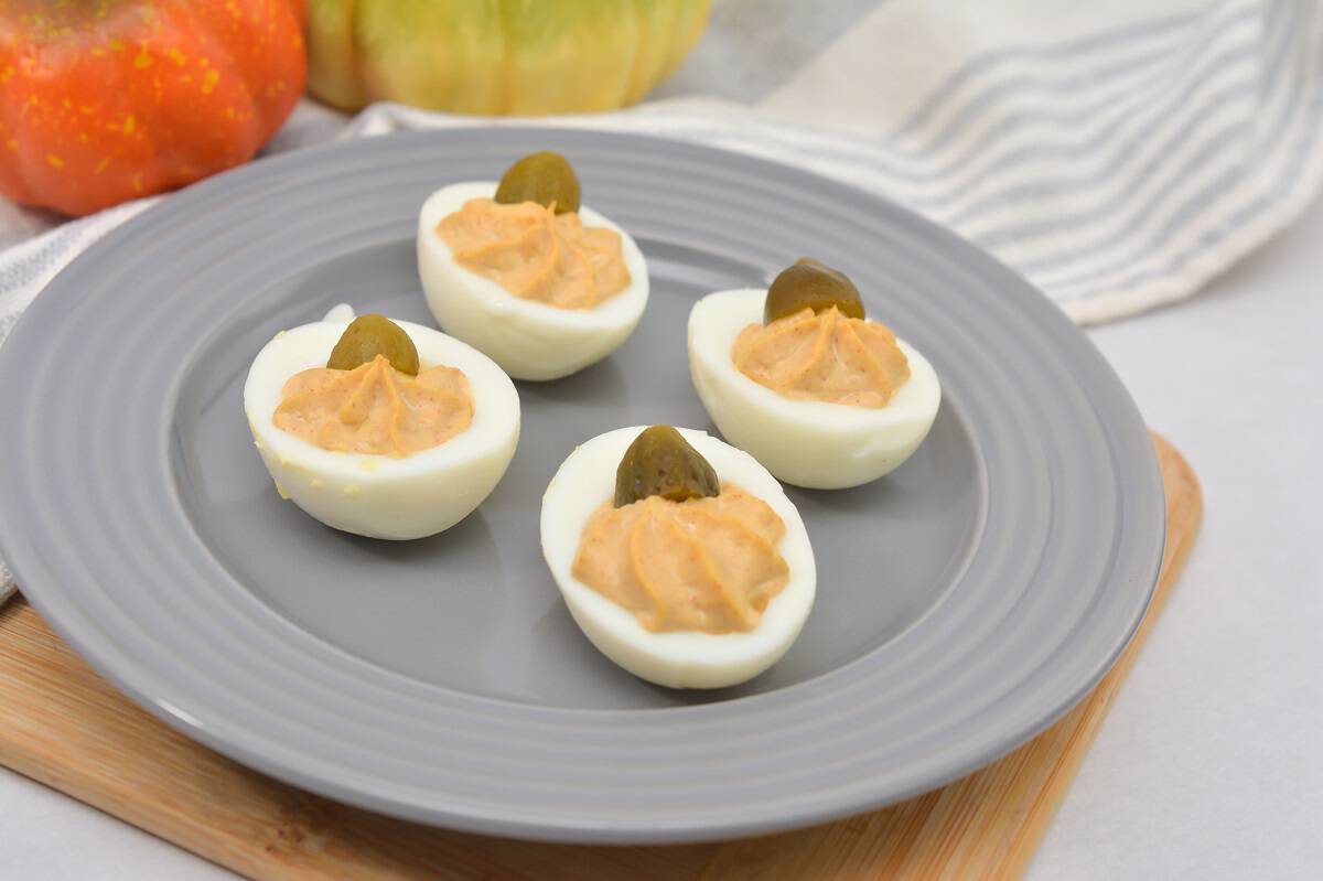 Four deviled eggs topped with pickles on a gray plate.