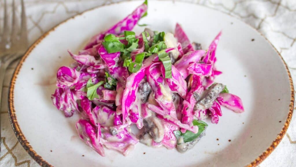 A plate of vibrant purple cabbage salad mixed with greens and sliced mushrooms, served on a rustic ceramic plate.