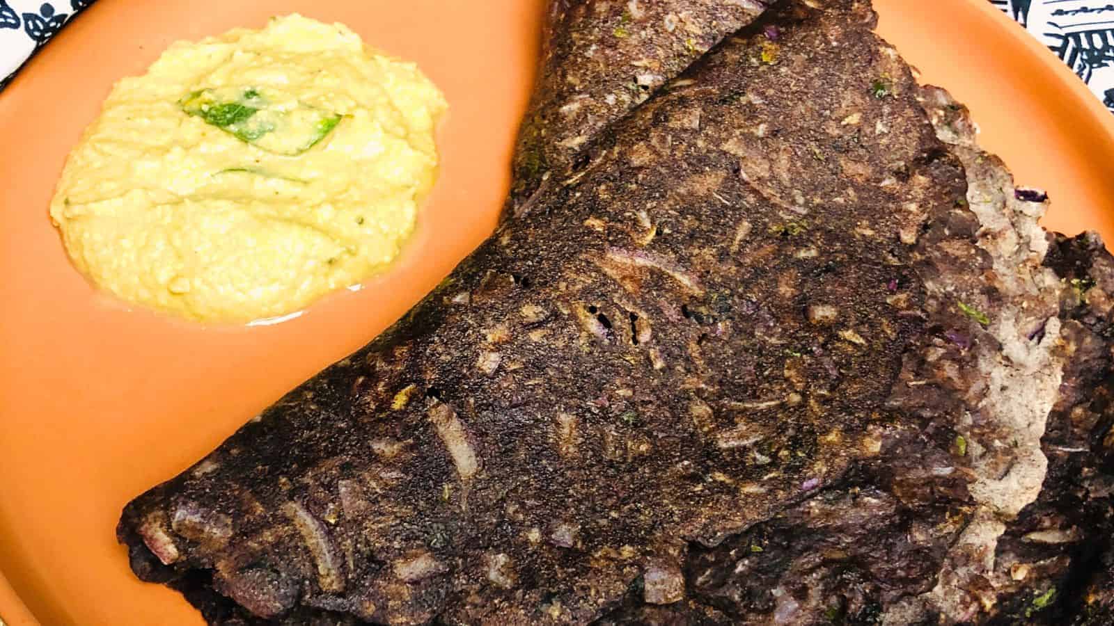 A Ragi Rotti served with a side of mashed yellow vegetables on an orange plate.