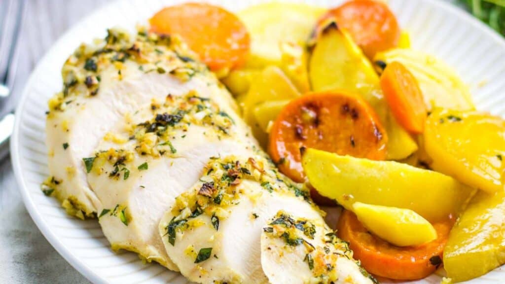 Herb-crusted chicken breast served with roasted yellow bell peppers and carrots.