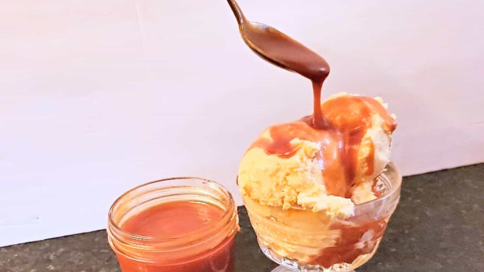 Image shows Caramel sauce being poured onto a scoop of vanilla ice cream in a glass bowl, with a jar of caramel sauce beside it.