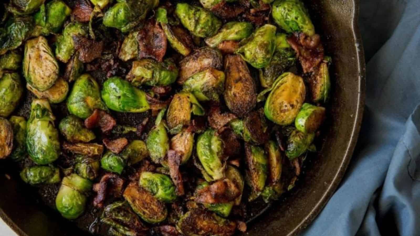 Sauteed Cast Iron Brussels Sprouts with Bacon in a white bowl with red pepper flakes, a spoon, and a fork.