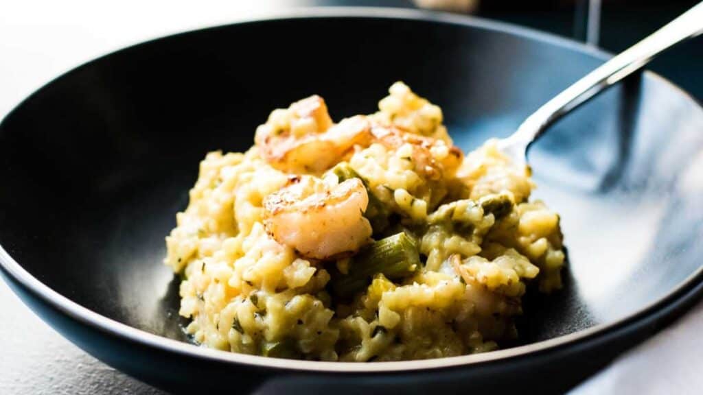 A plate of shrimp risotto with asparagus served on a black dish.