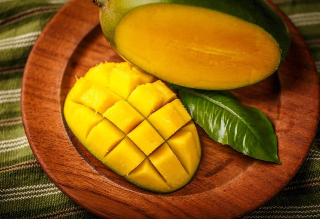 A ripe mango cut into cubes on a wooden plate with a green leaf for decoration.