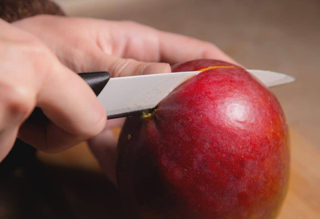 A person slicing a red apple with a knife.