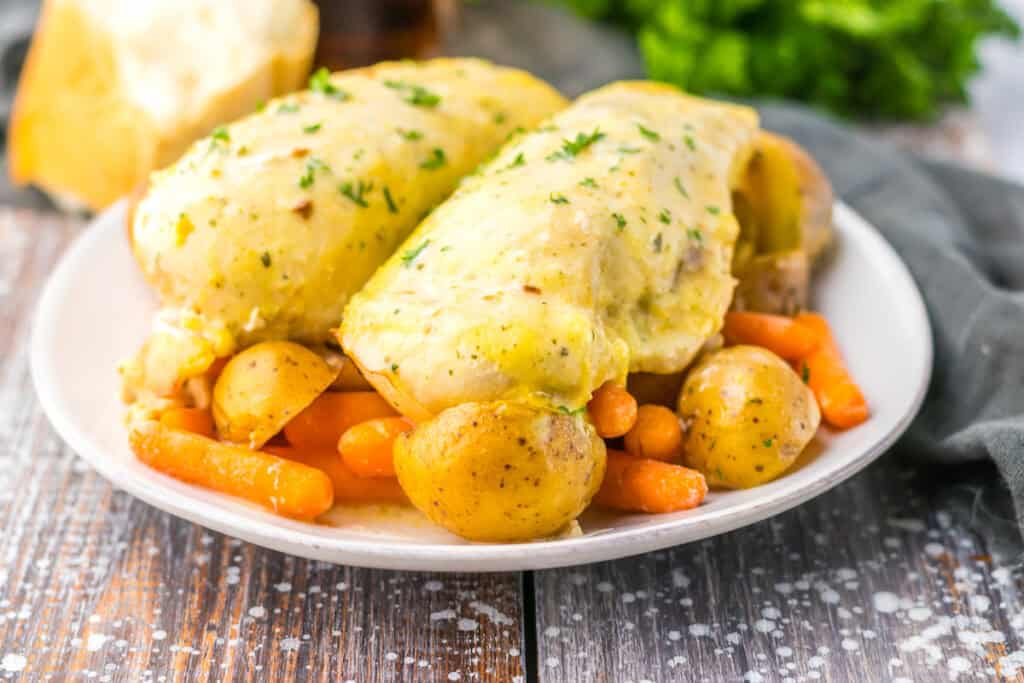 A plate of chicken breasts topped with creamy sauce, accompanied by boiled potatoes and carrots, garnished with herbs.