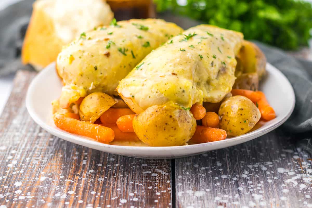 Plate of chicken with a creamy sauce, served with potatoes and carrots, garnished with parsley.