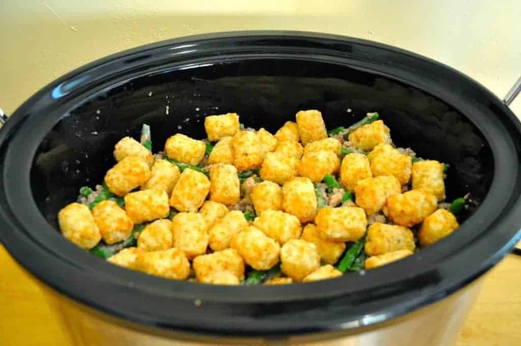 A slow cooker filled with tater tots and green beans, on a kitchen counter.