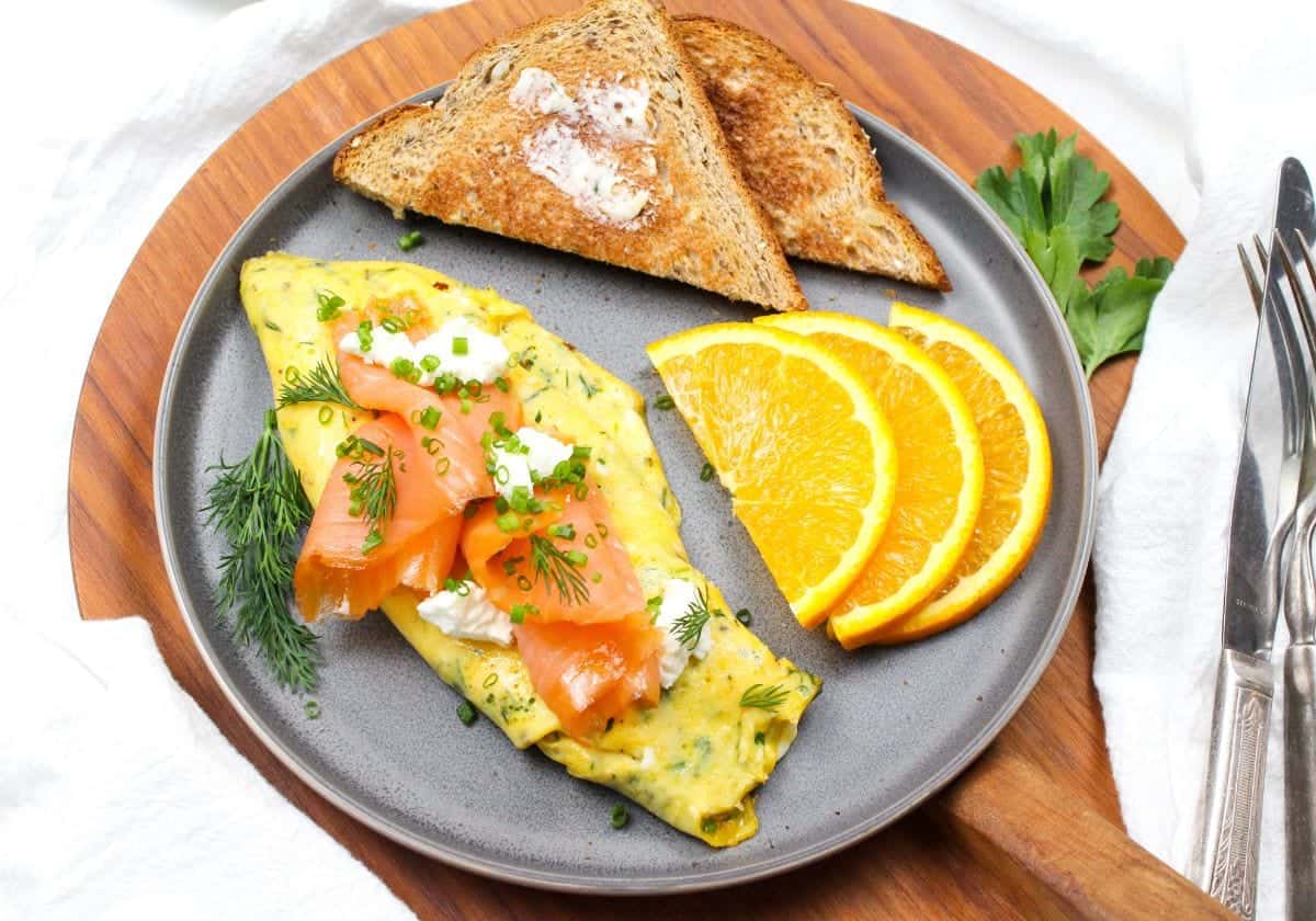 An omelette with smoked salmon and goat cheese on a plate with toast and orange slices.