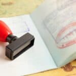A passport with entry stamps and a rubber stamp lying on a map, symbolizing international travel.
