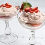 Two glass bowls of strawberry mousse topped with fresh strawberry slices on a white wooden table.