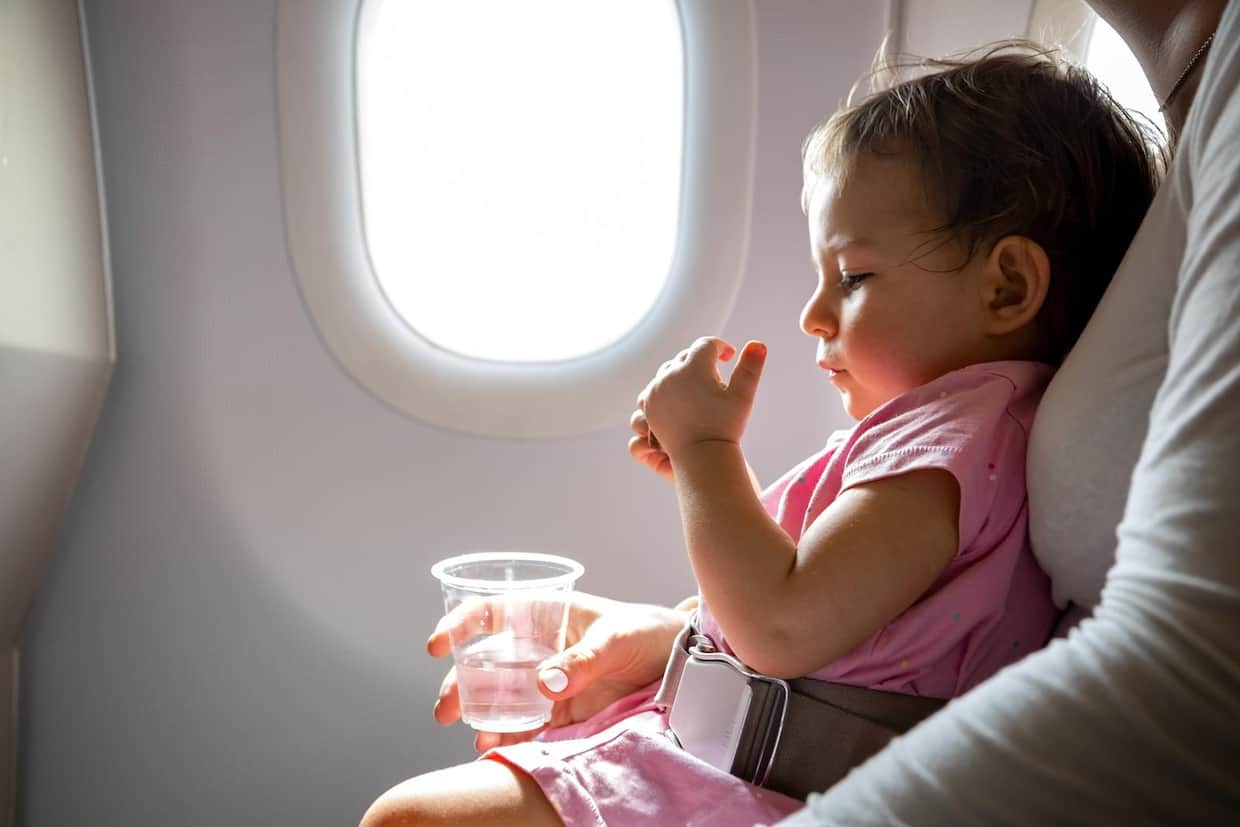 Toddler girl sitting on her mother's lap in an airplane. 