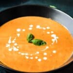 A bowl of creamy tomato soup garnished with fresh basil leaves and a swirl of cream.