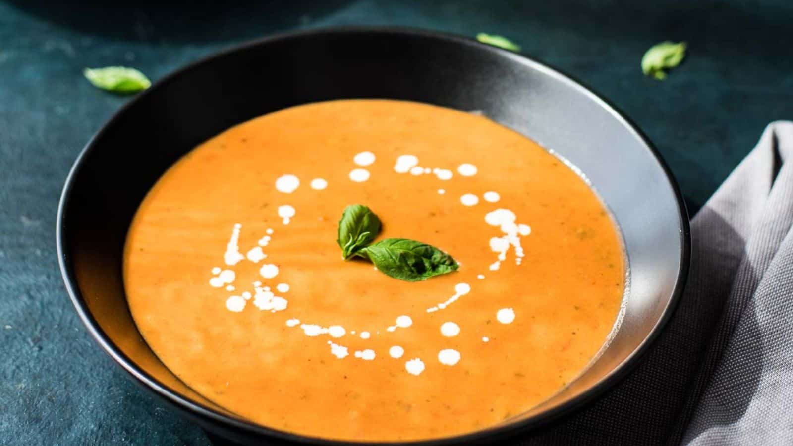 Two black bowls of tomato basil bisque on a blue background.