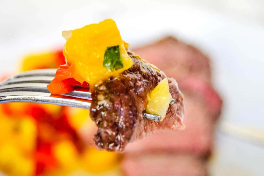 Close-up of a fork holding a piece of beef with colorful bell peppers, with a blurred background.